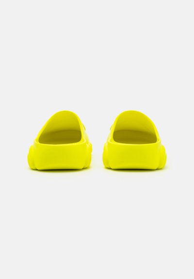 Zuecos amarillos brillantes de plástico brillante con apertura en la parte trasera y punta redondeada, con un diseño sencillo y textura suave.