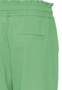 Zielone spodnie z elastycznym paskiem i jedną tylną kieszenią wpuszczaną, ukazujące górną część bioder i talii na białym tle.