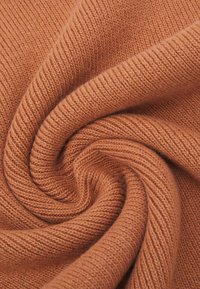 Tissu tricoté d'une teinte orange rouille chaude, présentant une texture côtelée avec une finition douce et lisse, disposé en un motif tourbillonnant.