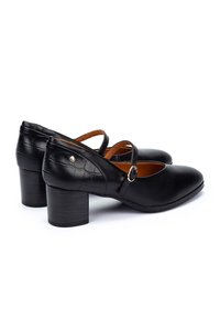 Talons en cuir noir avec un bout rond, comportant une bride croisée et un dos texturé. Le talon est cylindrique et de hauteur moyenne. Accent en matériel doré.