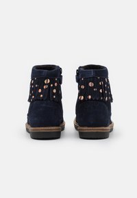 Bottines en daim bleu marine avec des accents en franges et des détails métalliques à pois, avec une semelle brune contrastante et une fermeture éclair.