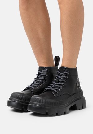 Schwarze Leder-Stiefeletten mit klobiger Sohle, grauen Schnürsenkeln und dekorativen Nieten an der Seite. Geriffelte Gummisohle für besseren Halt.