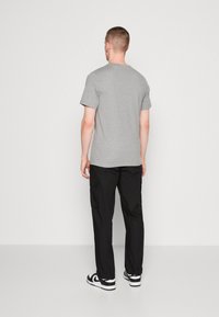 Tricou gri din bumbac cu mâneci scurte, asortat cu pantaloni cargo negri cu buzunare laterale și adidași negri cu alb. Design simplu.