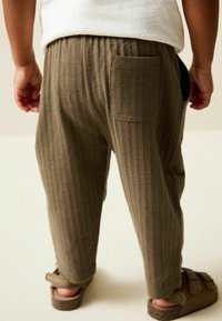 Khaki ribbed trousers with elastic waistband, side pockets, and a back pocket; textured fabric; worn with brown sandals.