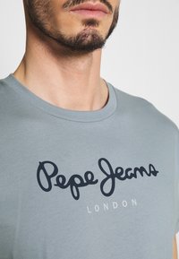 Grijze katoenen t-shirt met een ronde hals en korte mouwen, met een donkerblauwe logo tekst "Pepe Jeans LONDON" over de voorkant.