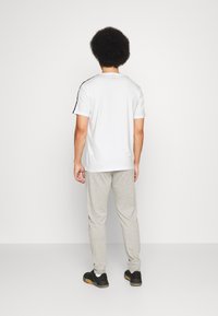 Hvid sportstrøje med sorte sidelændere, parret med lysegrå sweatpants. Outfittet inkluderer sorte sneakers.