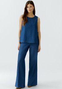 Denim-Zweiteiler bestehend aus einem ärmellosen Oberteil und weitem Hosenbein in einem mittleren Blauton, mit lockerer Passform und seitlichen Bindedetails.