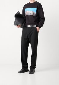 Černá mikina s barevným grafickým motivem, černé kalhoty, kožené psaníčko a černé boty. Pásek má stříbrnou obdélníkovou přezku.