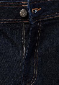 Jean en denim bleu foncé avec coutures orange, bouton en métal marqué "WMC JEANS" et braguette partiellement ouverte.