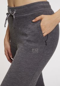 Gray ribbed joggers with a drawstring waist, side pocket, and embroidered “FC 1872” logo in a lighter gray. Soft texture, casual fit.