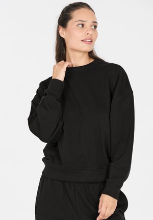 Schwarzer Pullover aus weichem Stoff, mit lockerer Passform, langen Ärmeln, gerippten Bündchen und Rundhalsausschnitt. Glatte Textur überall.