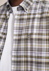 Karierte Hemd in Grautönen, Weiß, Gelb und Lila. Hergestellt aus einem leichten Stoff mit einem Button-Down-Kragen und einer Brusttasche.