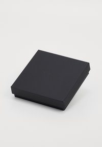 Fekete, matt bevonatú téglalap alakú doboz, enyhén megemelt fedéllel és a tetején dombornyomott márkanevével. Sima felület, minimalista dizájn.