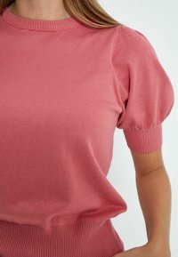 Maglione rosa lavorato a maglia con scollatura tonda a coste, maniche corte a sbuffo e orlo a coste. Il tessuto sembra morbido con una superficie liscia.