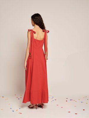 Abito maxi rosso con spalline legate a fiocchi, una parte superiore aderente e un orlo svasato. Presenta dettagli floreali vicino alle spalline.