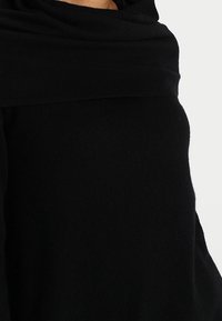 Écharpe noire en tricot avec une texture douce, drapée lâchement autour du cou, présentant une finition lisse et sans motifs ni éléments visibles.