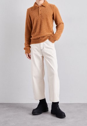 Maglione marrone peloso con colletto, pantaloni bianchi a gamba larga con cuciture a contrasto e stivaletti neri con suola testurizzata.