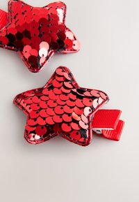 Red star-shaped clips covered in shiny sequins, featuring a smooth texture and a red ribbon attachment loop.