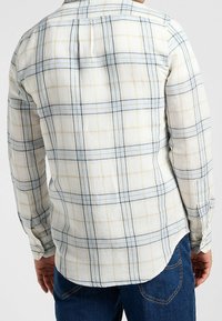 Camisa de manga larga de tejido ligero con cuadros azul y beige, puños con botones, bajo curvo y cuello estándar.