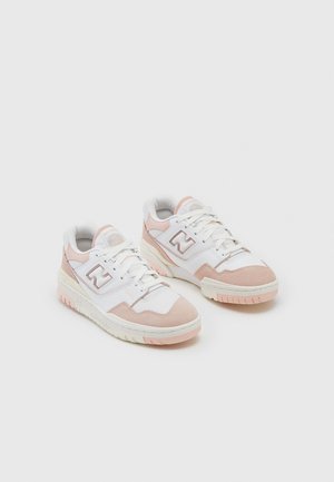 Para białych i jasnoróżowych sneakersów New Balance ze sznurowadłami, zamszowymi akcentami i gumowymi podeszwami na jednolitym jasnym tle.