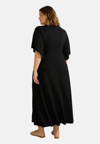 Robe maxi noire avec des manches volantées, corsage ajusté et jupe fluide. Tissu doux avec une texture lisse. La vue arrière montre des coutures minimales.