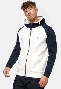Sudadera con capucha y cremallera, con un cuerpo blanco y mangas azul marino, tela texturizada, cordones ajustables y bolsillos canguro frontales.