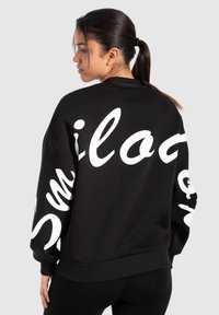 Felpa nera con testo bianco oversize in scrittura sul retro e sulle maniche. Presenta orli e polsini a coste, realizzata in un tessuto morbido.