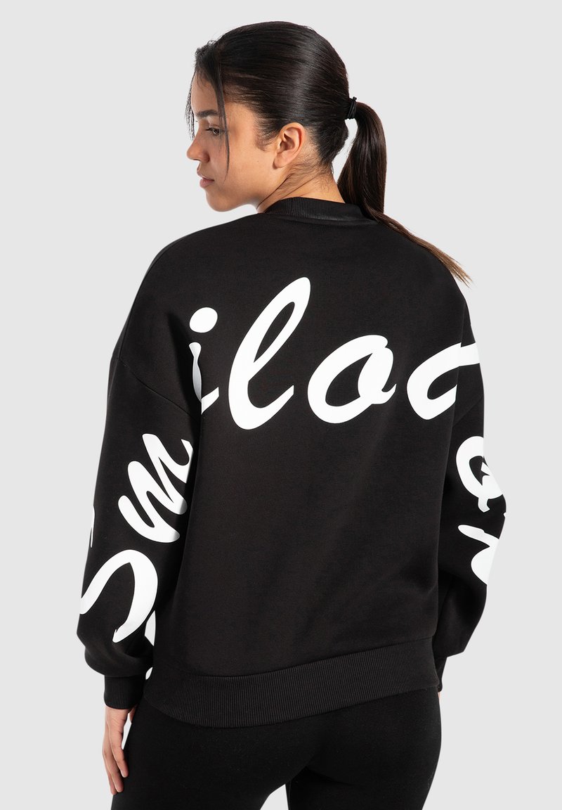 Felpa nera con testo bianco oversize in scrittura sul retro e sulle maniche. Presenta orli e polsini a coste, realizzata in un tessuto morbido.
