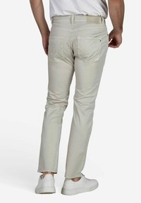 Lichtbeige rechte broek met een zachte textuur, voorzien van twee achterzakken en een subtiel logo op de tailleband. Gecombineerd met witte sneakers.