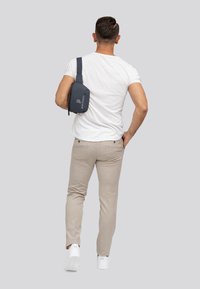 Donkerblauwe schoudertas met een gladde textuur en logo, gedragen over de schouder; gecombineerd met lichtbeige broek en witte sneakers.