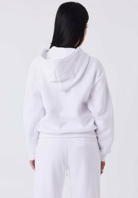 Witte hoodie met een relaxte pasvorm, voorzien van ribgebreide manchetten en een textuurstof. Achteraan is de capuchon en de verstelbare koordjes zichtbaar.