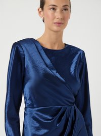 Tengerészkék ruha fényes anyagból, hosszú ujjakkal és átlapolt nyakkivágással, derékrészen ejtett redőkkel és oldalsó pliszírozással.