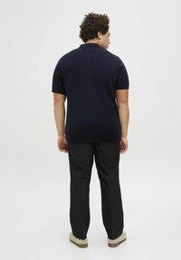 Navy spalvos trumpomis rankovėmis polo marškiniai su tekstūruotu mezgimu, derinami su juodomis kelnėmis ir šviesiais batais. Paprastos, švarios linijos ir klasikinis siluetas.