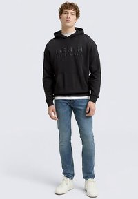 Hanorac negru cu inscripția „DENIM” în relief pe față, buzunar tip cangur și manșete tricotate, purtat peste un tricou alb și asortat cu blugi albastre deschis.