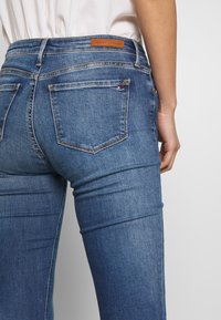 Blauwe denim jeans met een aansluitend ontwerp, voorzien van een tan leren logo patch en twee achterzakken, waarvan er één is geaccentueerd met de kleuren van het merk.