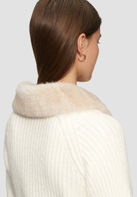 Weißer gerippter Pullover mit einem weichen, beigen Pelzkragen, der einen lässigen Schnitt und dezente Details an den Schultern und Ärmeln aufweist.