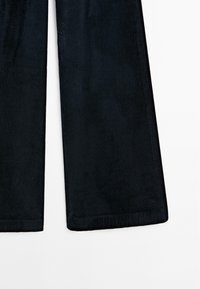 Zwarte corduroy broek met wijde pijpen, voorzien van een verticale ribbelstructuur en gestikte zoom. De stof lijkt zacht en licht glanzend.