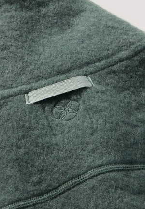 Grünes, filzartiges Wollprodukt mit einer Textur aus weichen Fasern, ausgestattet mit einer genähten Naht und einem kleinen, geprägten Logodetail.