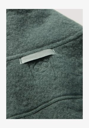 Grünes, filzartiges Wollprodukt mit einer Textur aus weichen Fasern, ausgestattet mit einer genähten Naht und einem kleinen, geprägten Logodetail.