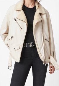 Giacca oversize color crema con colletto in finta shearling e numerose tasche con zip. Realizzata in tessuto morbido, presenta un design unico.