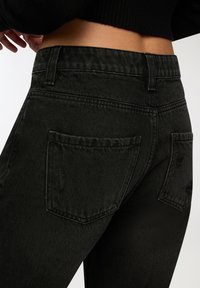 Czarne dżinsy o dopasowanym kroju, z dwoma tylnymi kieszeniami i subtelnymi przetarciami. Teksturowany materiał o lekko połyskującej powierzchni.