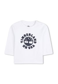 Witte katoenen overhemd met korte mouwen, voorzien van een marineblauw, rond Timberland-logo met een boomafbeelding en de tekst "NH USA." Twee drukknopen op de schouders.