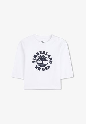 Biała bawełniana koszula z krótkim rękawem z granatowym okrągłym logo Timberland z grafikiem drzewa i napisem "NH USA". Dwa zatrzaski na ramionach.