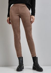 Leggings in suede marrone con una texture liscia e una vestibilità aderente, abbinati a stivaletti neri e a un maglione nero. Design semplice e moderno.