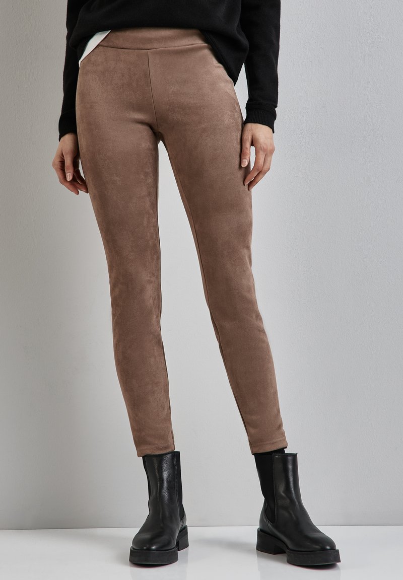 Leggings in suede marrone con una texture liscia e una vestibilità aderente, abbinati a stivaletti neri e a un maglione nero. Design semplice e moderno.