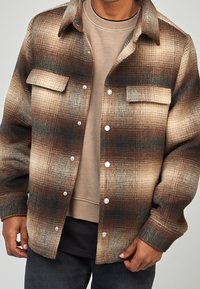 Rutigt skjortjacka i bruna och beiga nyanser, med krage, framfickor och silverfärgade tryckknappar. Texturerat ullmixmaterial.