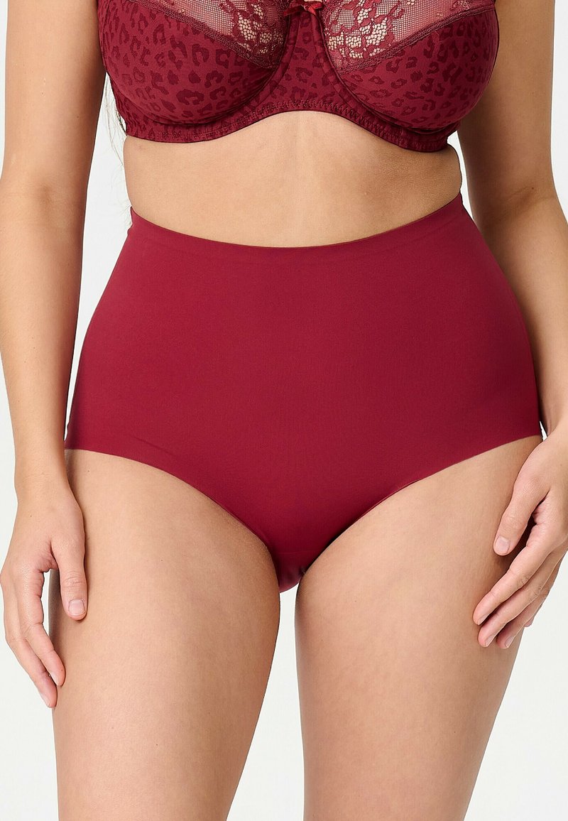 Femme portant des sous-vêtements rouges sans coutures taille haute et un soutien-gorge rouge assorti avec dentelle et détails imprimés léopard.