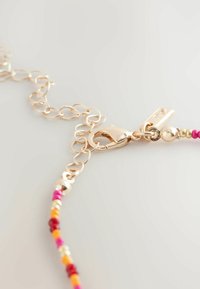 Multi-colored beaded bracelet with a gold-tone metal clasp, featuring small round beads in pink, orange, yellow, and red tones.