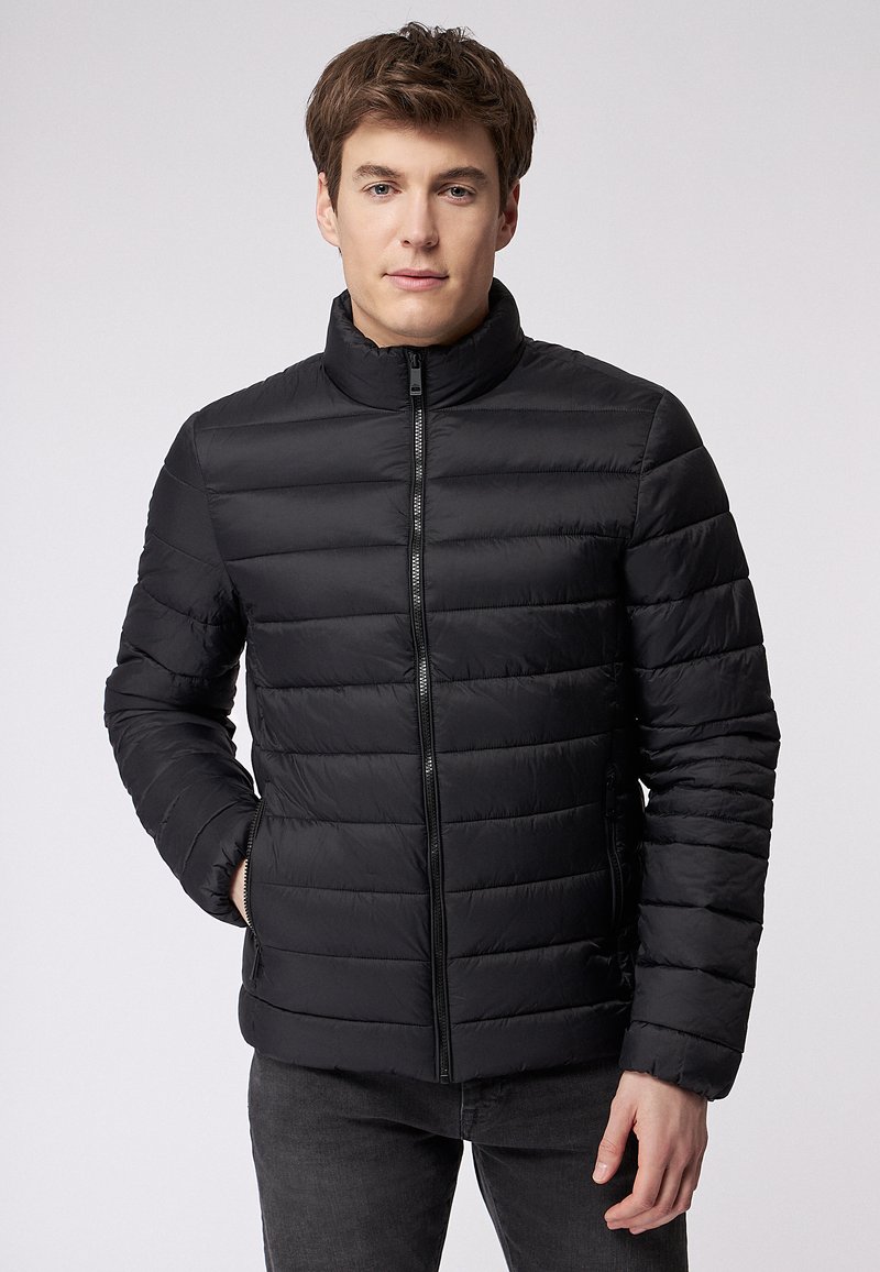 Giacca imbottita nera con colletto alto, chiusura frontale con zip e tasche laterali. Il design presenta sezioni trapuntate orizzontali e una superficie liscia.