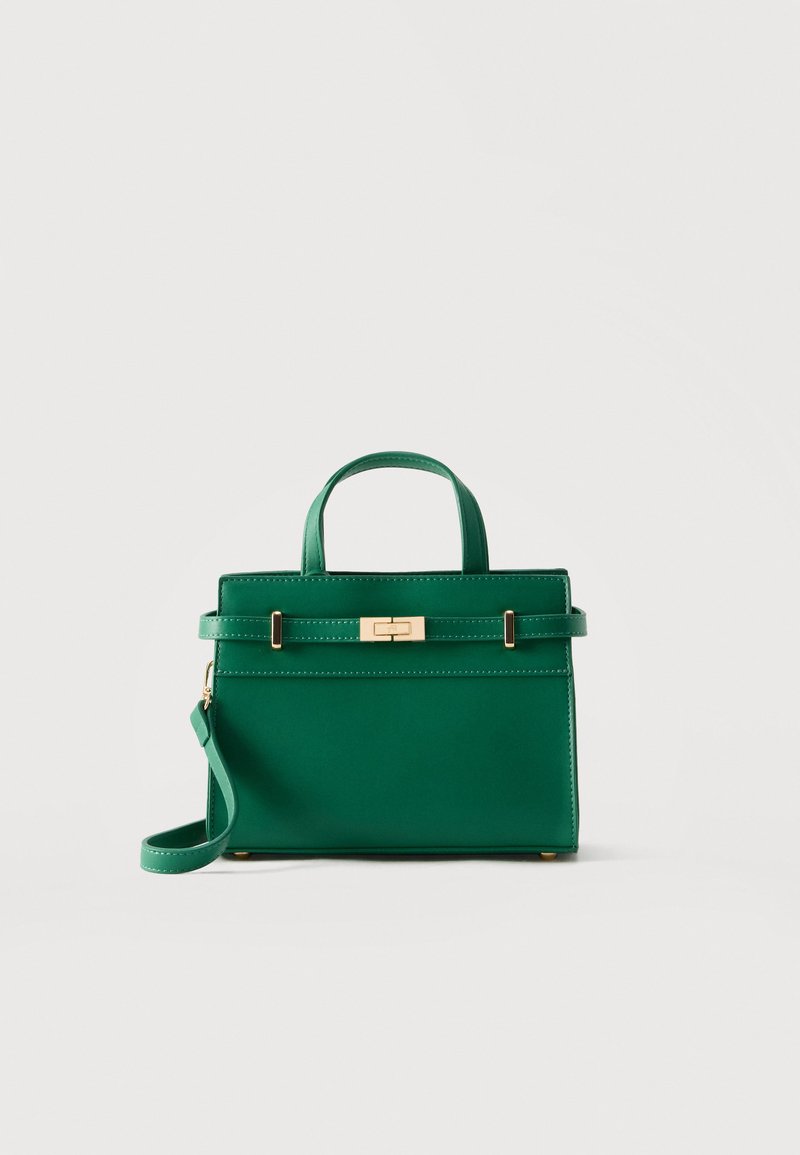 Πράσινη δερμάτινη τσάντα με χερούλι στο πάνω μέρος, κούμπωμα σε χρυσό τόνο και αποσπώμενο ιμάντα ώμου σε απλό ανοιχτό φόντο.